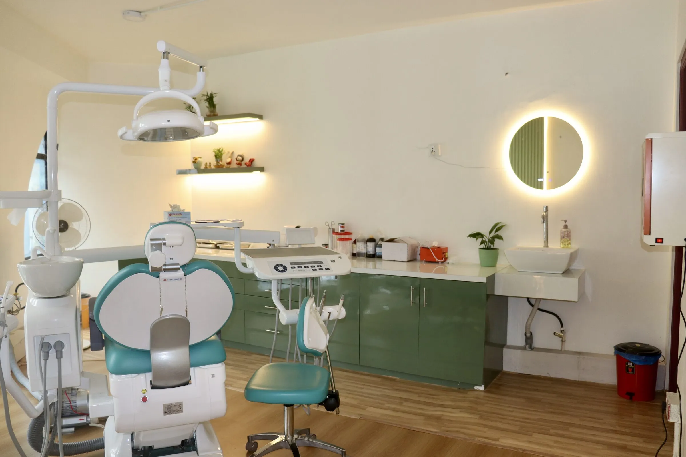 Treatment room with a teal dental chair and a round lit mirror